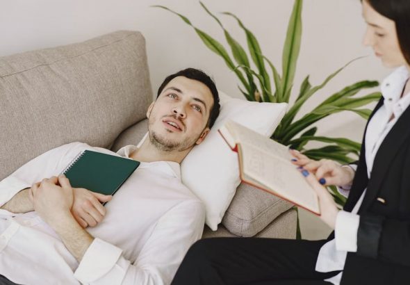 Thoughtful well dressed man with journal lying on sofa in office of modern female therapist and telling about problems