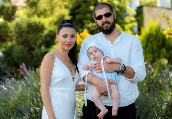 Charming family portrait of parents with a baby in a vibrant summer garden setting.